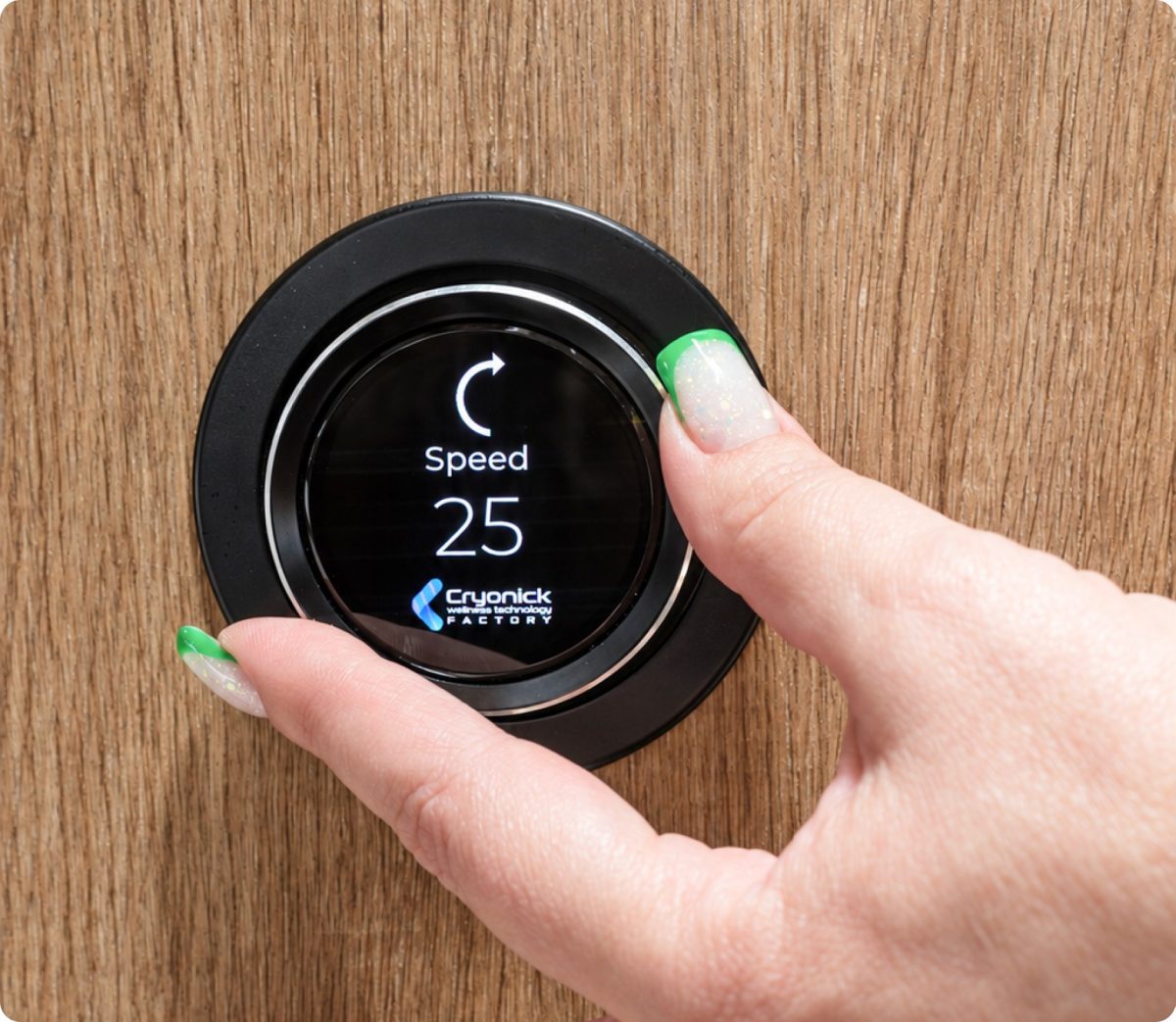 Close-up of a hand turning a small black circular device on a wooden surface, displaying 'Speed 25' on its screen with a white arc icon and branding beneath.